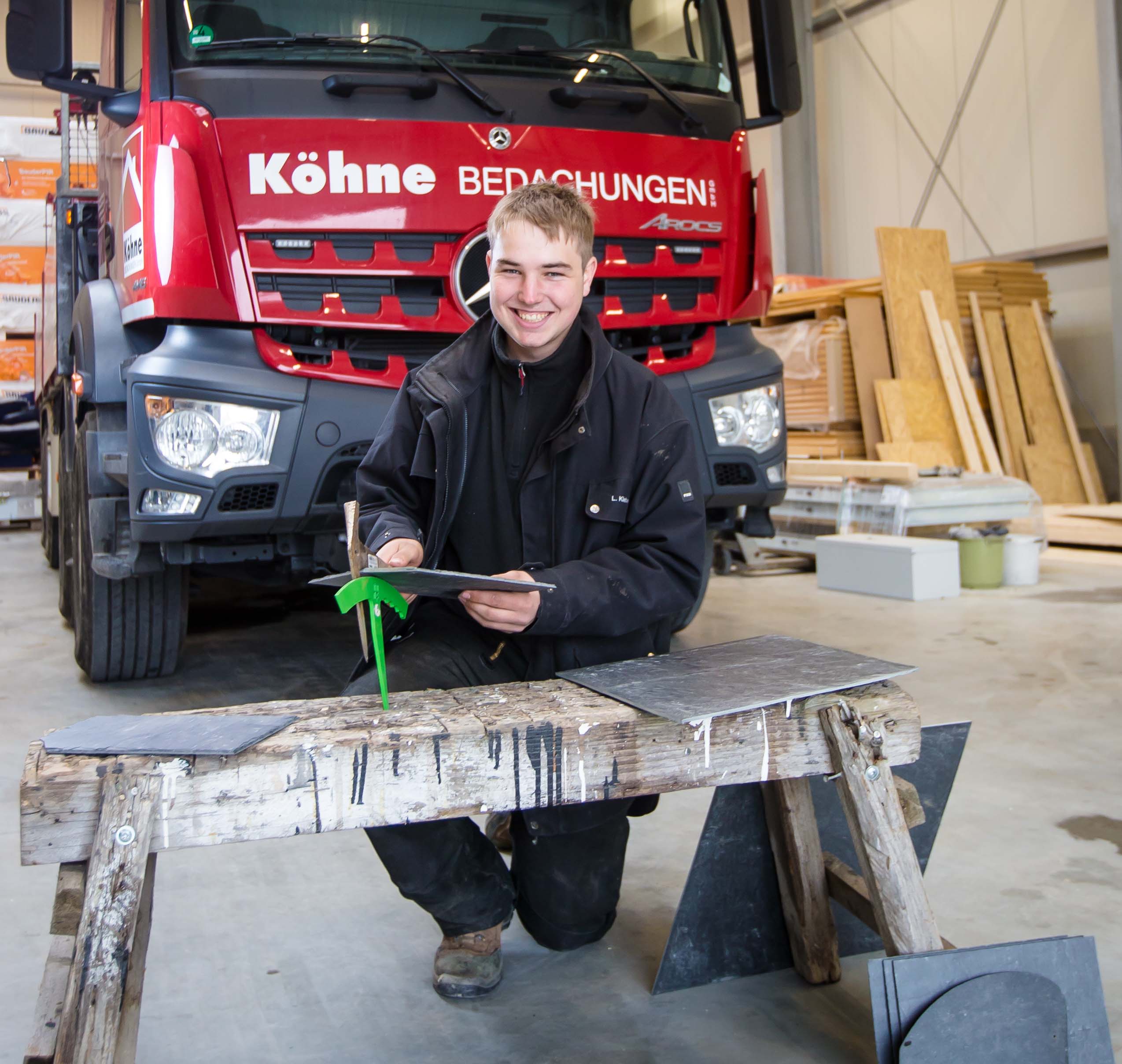 Der 16-jährige Auszubildende Luca Kleber bearbeitet eine Schieferplatte mit einem Schieferhammer und einer Haubrücke.