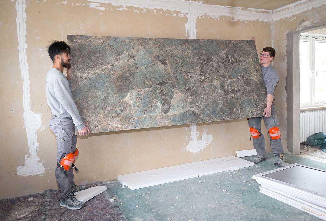 Fliesenleger Hadi Ibrahimi und Carl Mies halten eine große Fliesenplatte vor der Wand - Traumberufe Fliesen-, Platten- und Mosaikleger 2023