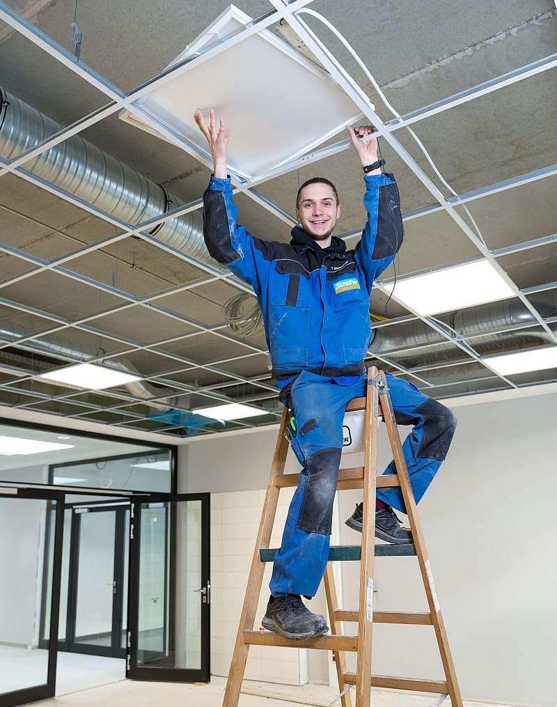 Torben Brinkmann steht auf dem Leiter und installiert die Deckenleuchten - Traumberufe Elektroniker und Informationselektroniker 2023
