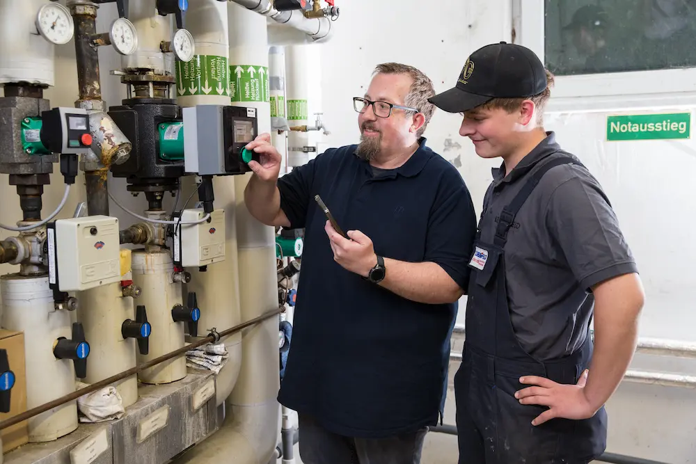 Installateur- und Heizungsbaumeister Bernd Liesenfeld (links) zeigt seinem Azubi Ben Aufderbeck, wie er diese Heizungsumwälzpumpe einjustiert und die Durchflussmenge präzise mit dem Handy steuert.

