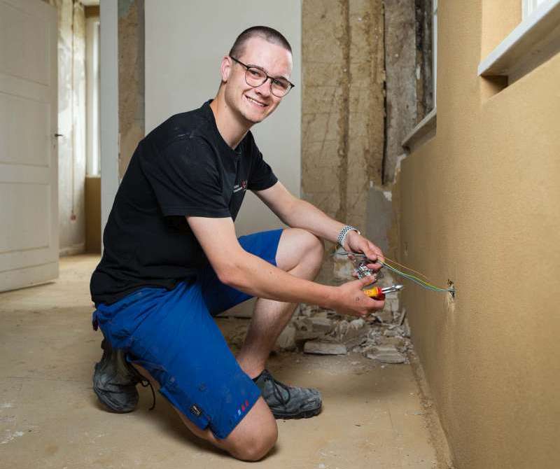Der angehende Elektroniker für Energie- und Gebäudetechnik installiert eine Steckdose an einer verputzten Wand. (Foto: Gabi Bender)