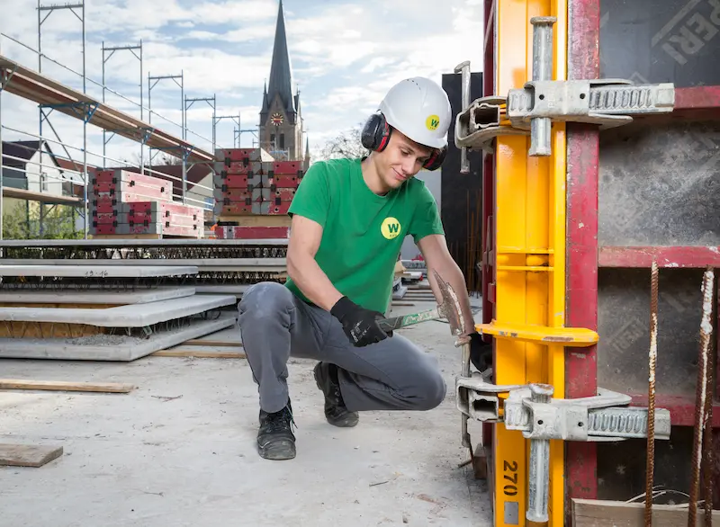 Für das Fixieren einer Klammer an einer Rahmenschalung für eine tragende Betonsäule trägt Maurer-Azubi Fabian Marks einen Gehörschutz. Traumberufe 2026 Maurer