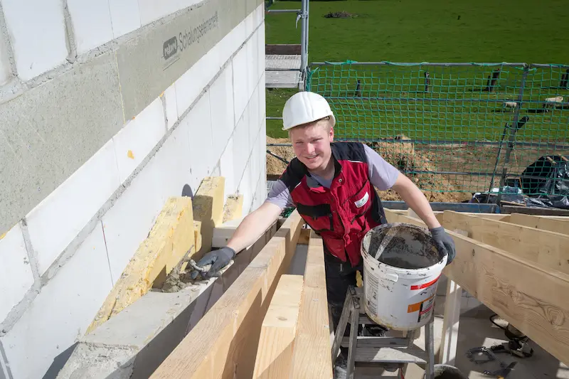 Azubi Simon Authmann trägt Mörtel auf einer Mauer auf. Traumberufe 2026 Maurer