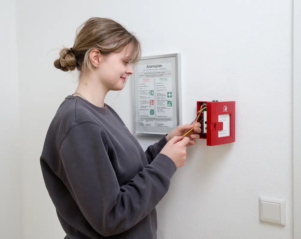 Jana Jochimsthal schließt einen Handdruckmelder einer Brandmeldeanlage an. Traumberufe 2026 Elektroniker