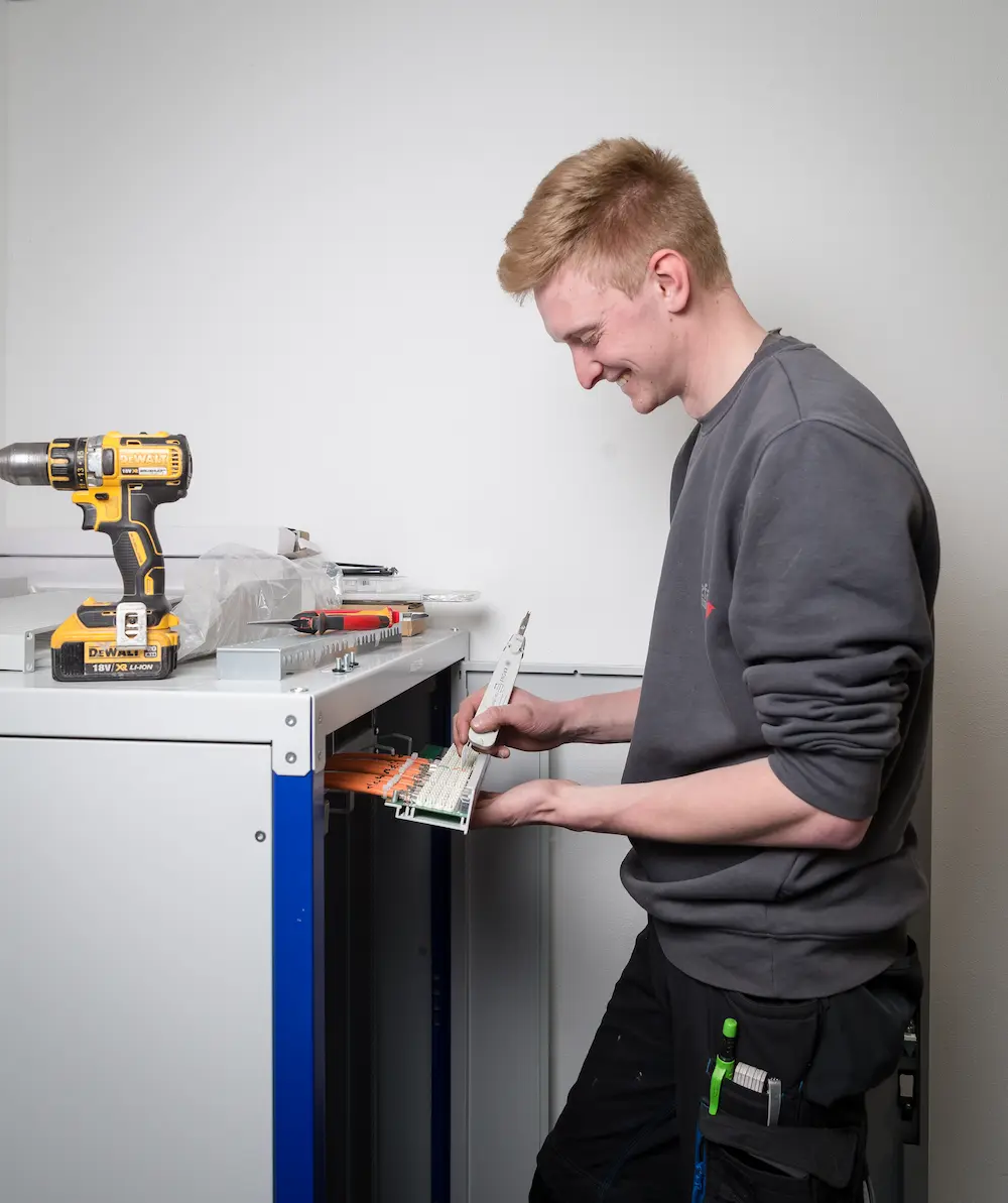 In einem Netzwerkschrank legt Lukas Mause fachgerecht Datennetzwerkleitungen auf ein Patchfeld auf. Traumberufe 2026 Elektroniker
