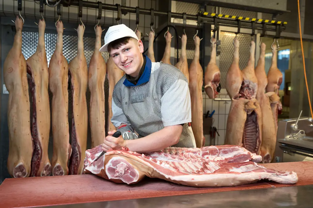 Mit einem Ausbeinmesser schneidet Fleischer-Azubi Lorenz Baumüller die Kotelettreihe aus dem halben Schwein heraus.
