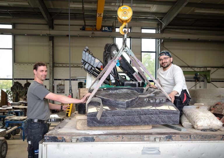 Meister Marcel Grundhöfer (links) und Azubi Schechmus Husen heben den Grabstein mit dem Kran - Traumberufe Steinmetz 2023