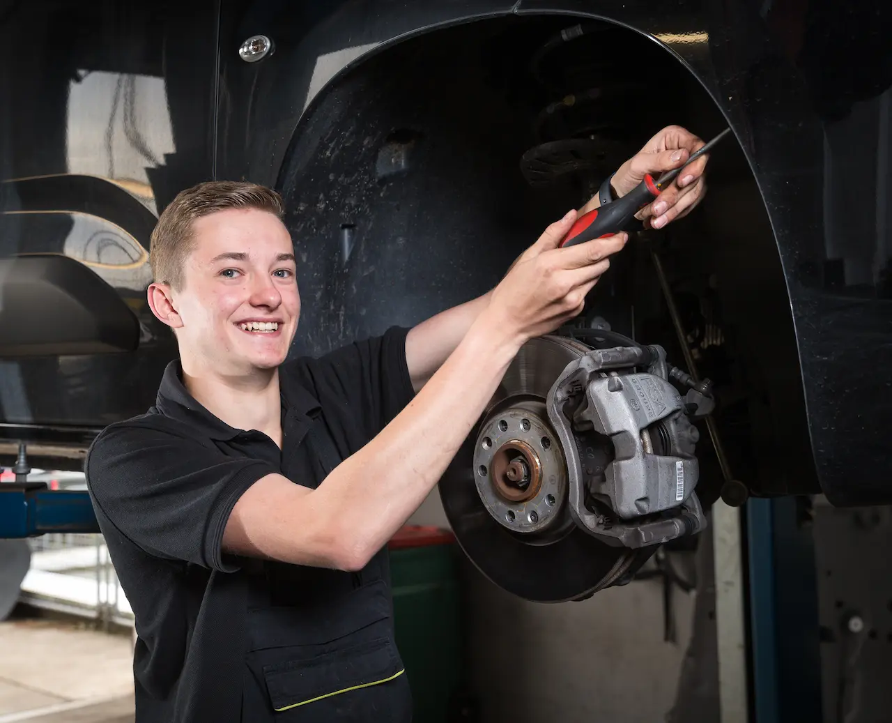 Vitus Hanfland, der eine Ausbildung zum Kfz-Mechatroniker macht, schraubt die Radhausschale eines Fahrzeugs ab, um den Riementrieb des Keilriemens überprüfen zu können.