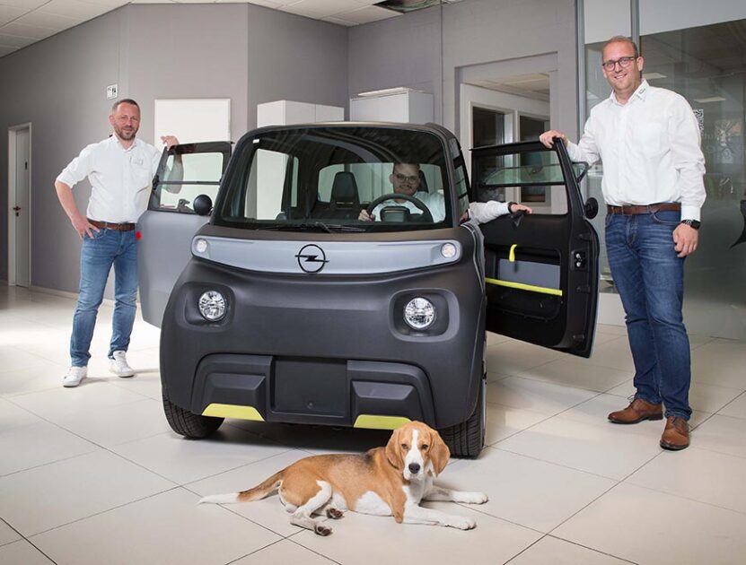 Justin Schnier-Winke, Azubi zum Automobilkaufmann im zweiten Lehrjahr, hat im neuen Rocks Electric von Opel, den bereits 15-Jährige fahren dürfen, Platz genommen. Eingerahmt wird das kompakte City-Mobil von Verkaufsberater Krzysztof Bregula (links), Geschäftsführer Alexander Regett sowie dem Beagle Hugo. (Foto: Gabi Bender)