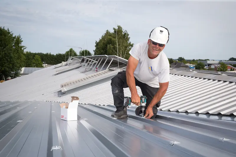 Jens Loose verschraubt die Sandwichpaneele auf dem Metalldach der Hallenerweiterung. Traumberufe Dachdecker 2026
