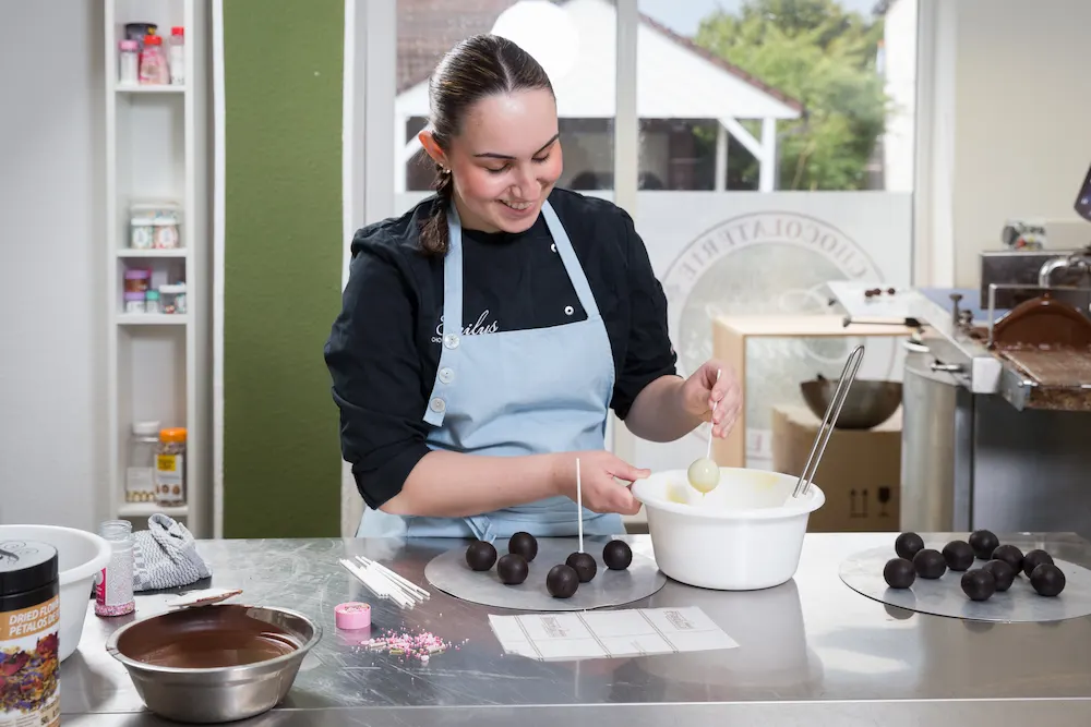 Die angehende Konditorin Anna Fevga taucht die Cake-Pops in weiße Schokolade, bevor sie aus diesen mit farbenprächtiger Deko kleine Kunstwerke kreiert.