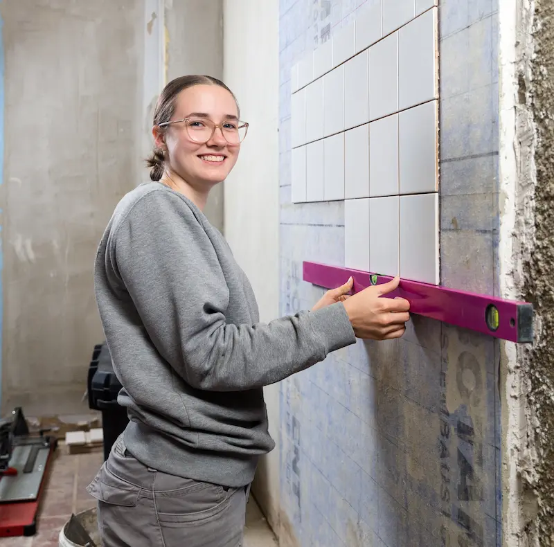 Laura Ramsel überprüft die Lage der Fliesen mit ihrer Wasserwaage. Traumberufe Fliesenleger 2026