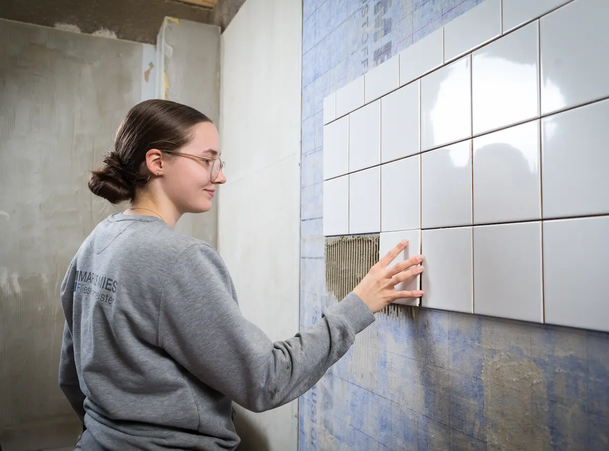 Laura Ramsel verlegt kleine weiße Wandfliesen. Traumberufe Fliesenleger 2026
