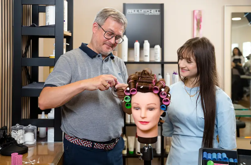 Friseurmeister Tim Wagener überprüft die von Nor Ali eingedrehten Haarsträhnen. Traumberufe Friseur 2026