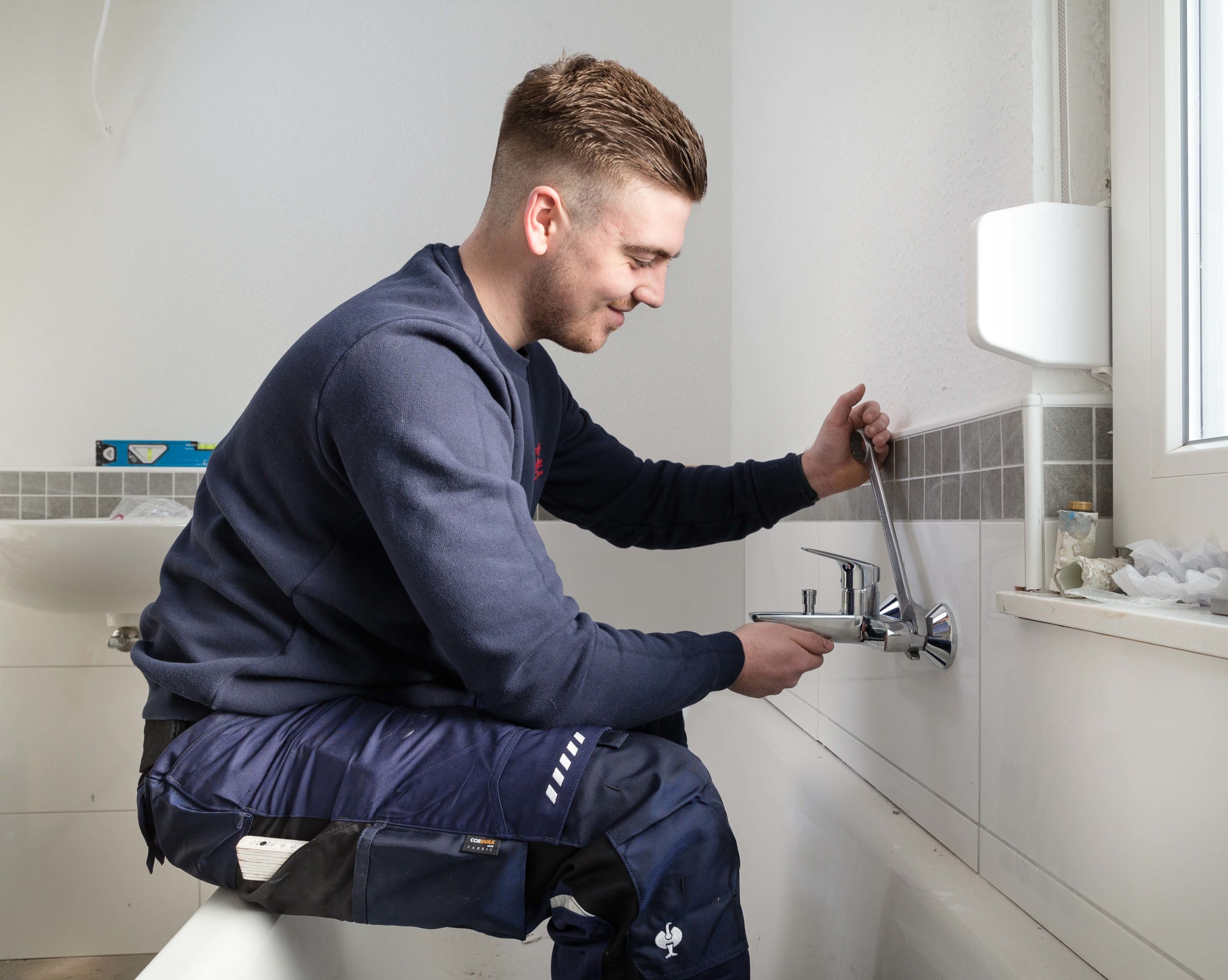 Sven Kössendrup justiert die Armatur einer Badewanne und schraubt sie fest - Traumberufe Anlagenmechaniker für SHK 2023