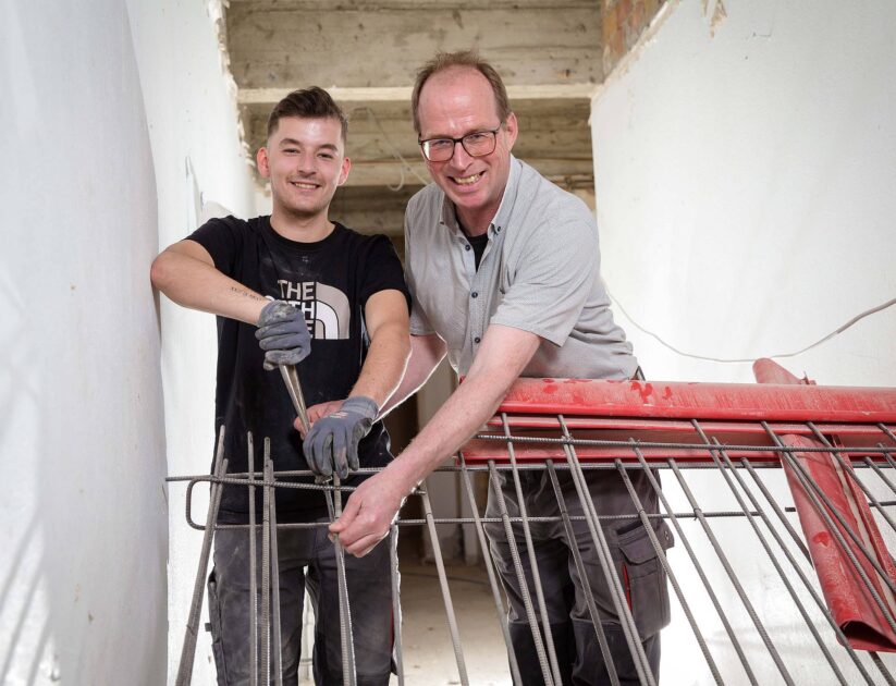 Geselle Luca Heidrich montiert gemeinsam mit Maurermeister Thomas Peveling ein Eisen an einen Querträger und baut so die Bewehrung für eine Stahlbetontreppe, die zwei Geschosse im Hubertus-Schwartz-Berufskolleg in Soest miteinander verbinden soll. Foto: Gabi Bender