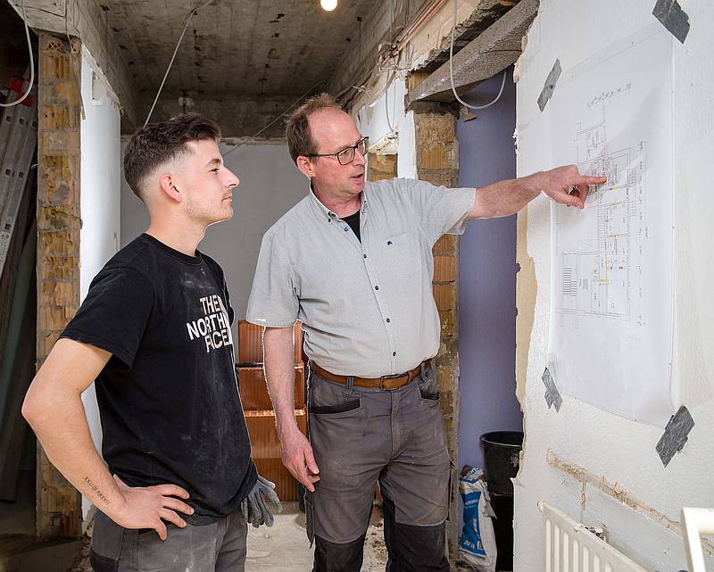 Auf dem Grundriss zeigt Maurermeister Thomas Peveling dem Gesellen Luca Heidrich, welche Türöffnungen zugemauert werden und wo für neue Zugänge Mauern eingerissen werden müssen. Foto: Gabi Bender