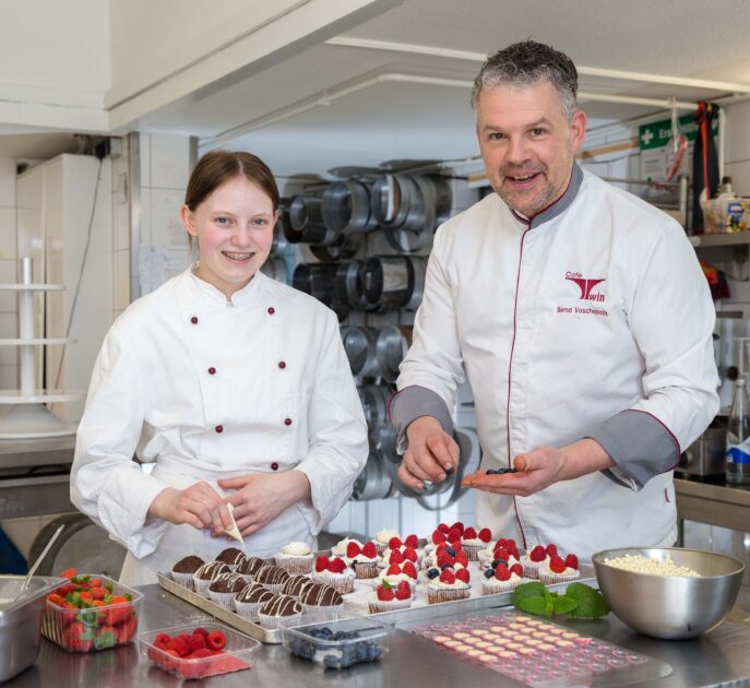 Die angehende Konditorin Liane Zilke und Konditormeister Bernd Voschepoth garnieren gemeinsam Waldfrucht-Cupcakes und Schokoladen-Muffins für eine Hochzeitsfeier. Foto: Gabi Bender