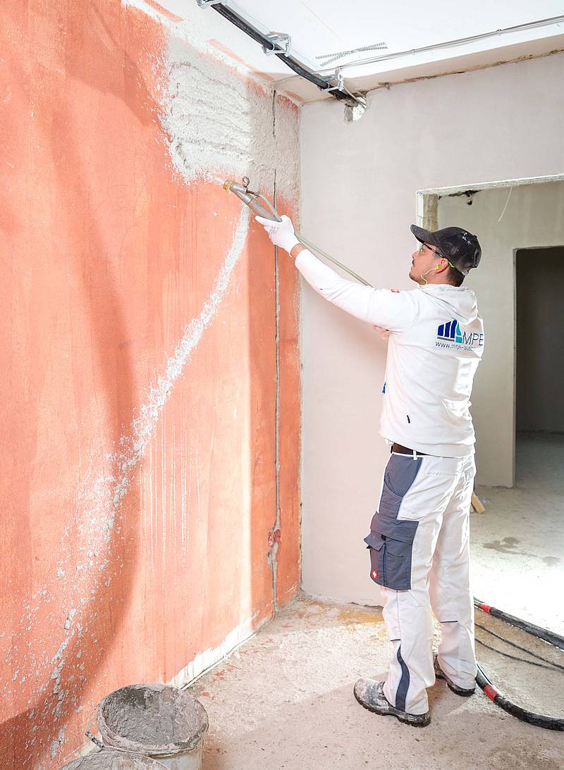 Stuckateur Rene Egbers spritzt mit einer Putzmaschine Gipsputz an eine Wand. Foto: Gabi Bender