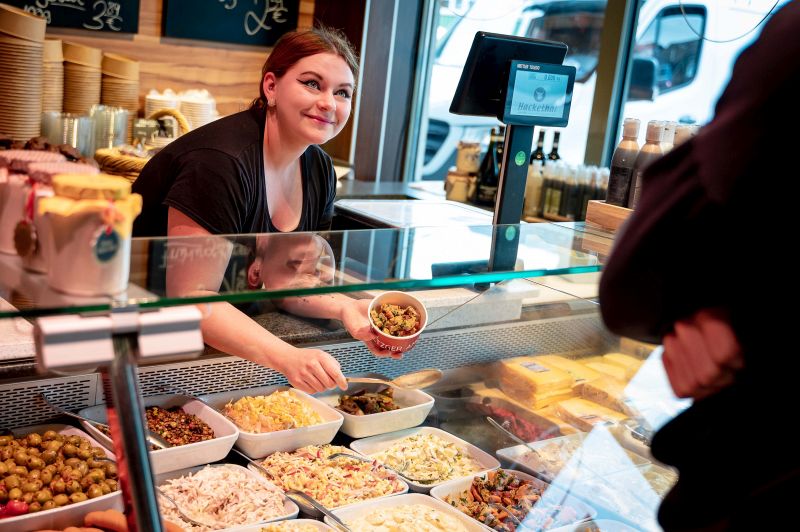 Fleischereifachverkäuferin Nadine Otterstedde füllt für einen Kunden Schweinefiletsalat mit Süßkartoffeln und getrockneten Tomaten ab. (Foto: Jorge Design)