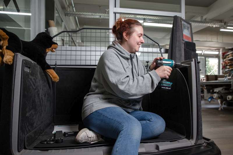 Mit einem Akkuschrauber schraubt Wendy Grefe die Halterung für den Kofferraumschutz an die Verkleidung - Traumberufe Raumausstatter, Sattler und Schneider 2023