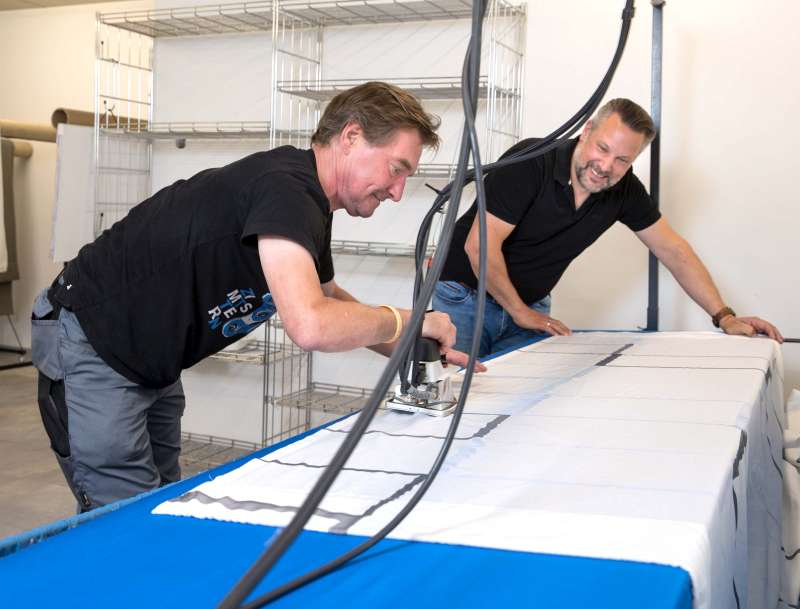Stephan Limper und Michael Richter bügeln am großen Bügeltisch eine Gardine - Traumberufe Raumausstatter, Sattler und Schneider 2023