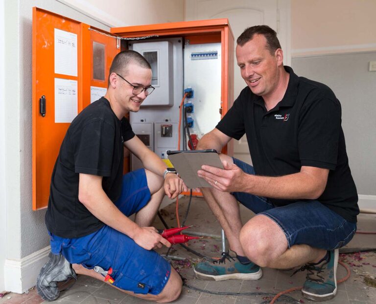 Vor dem Baustromverteiler bespricht Elektronikermeister und Geschäftsführer Dominik Esken mit dem Auszubildenden Fabian Immich den E-Check. (Foto: Gabi Bender)